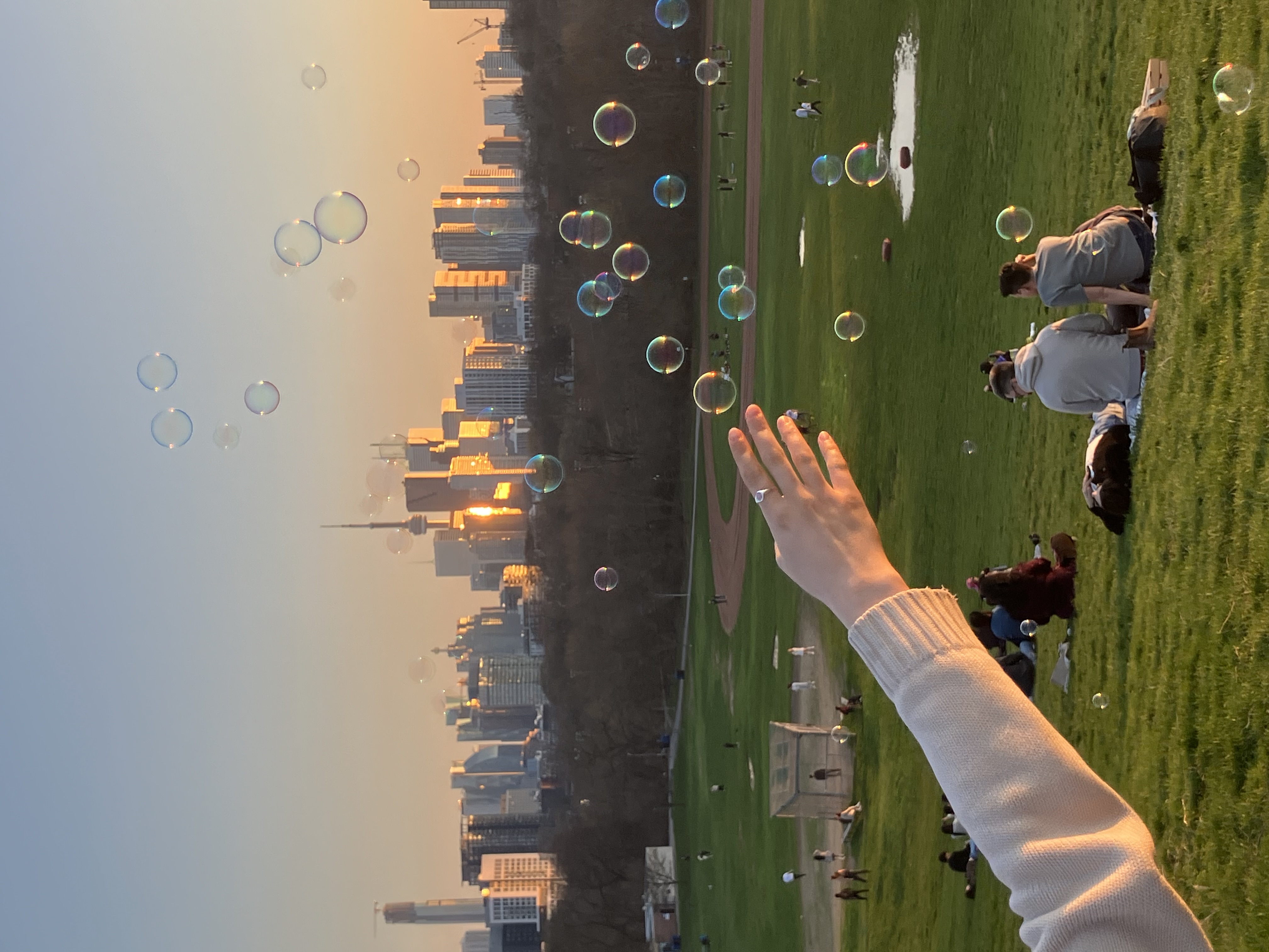 Toronto skyline at sunset, a hand stretching out in the foreground from the left, with bubbles floating through the air